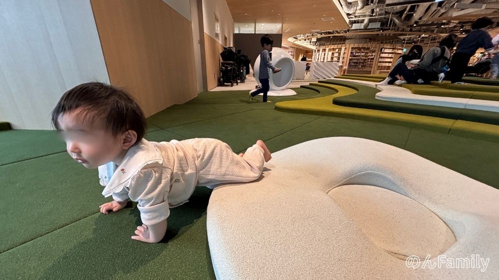 NEWoMan高輪South 5階にある無料の遊び場「PARK フレルト」。緑のクッションフロアが広がる空間で、靴を脱いで裸足でハイハイを楽しむ赤ちゃんの様子。歩けない小さい子供も安心して遊べる安全な環境。