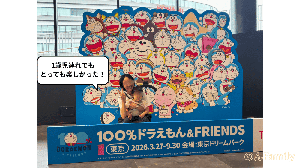 「100％ドラえもん＆FRIENDS（東京ドリームパーク）」のフォトスポットの前で、1歳児の娘を抱っこして笑顔で記念撮影をする親子の写真。「1歳児連れでもとっても楽しかった！」という吹き出しの文字が入った、子連れお出かけレポの冒頭画像。