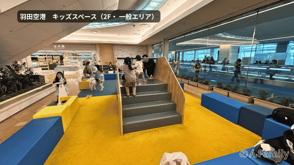 羽田空港第2ターミナル2階の一般エリアにあるキッズスペース。黄色いカーペットに青いソファ、中央に小さな滑り台や階段の遊具があり、子どもたちが遊んでいる様子
