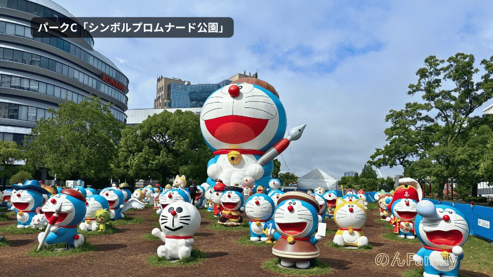 「100％ドラえもん＆FRIENDS（東京ドリームパーク）」の有料エリア、パークC「シンボルプロムナード公園」。ウッドチップが敷かれた広場に並ぶ多数のドラえもんフィギュアと、中央にそびえ立つ全長12mの巨大ドラえもんバルーン。