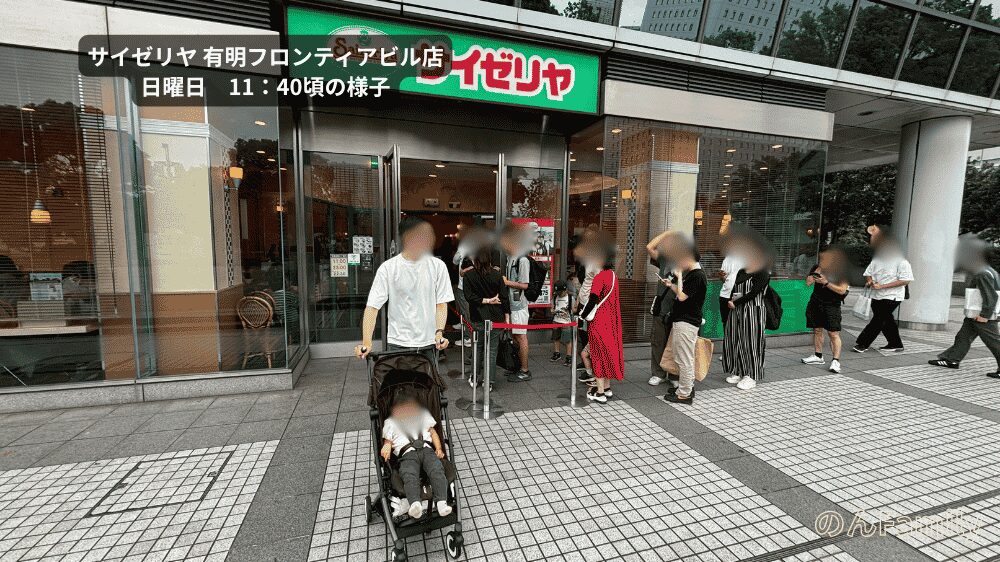 日曜日11時40分頃のサイゼリヤ有明フロンティアビル店の外観と、店外にできている入店待ちの行列。手前にはベビーカーに乗った1歳児の娘と見守るパパが写っており、お台場・有明エリアの子連れランチの混雑状況がわかる写真。