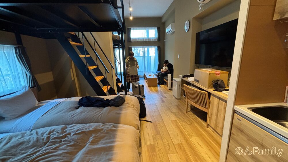 VILLA KOSHIDO ODORIの客室「Kyoto-JAPANESE Modern-B」の広々とした内観。低いベッド、2段ベッド風のロフト階段、テレビ、事前に郵送された段ボール箱が置かれたデスクがある木目調の部屋
