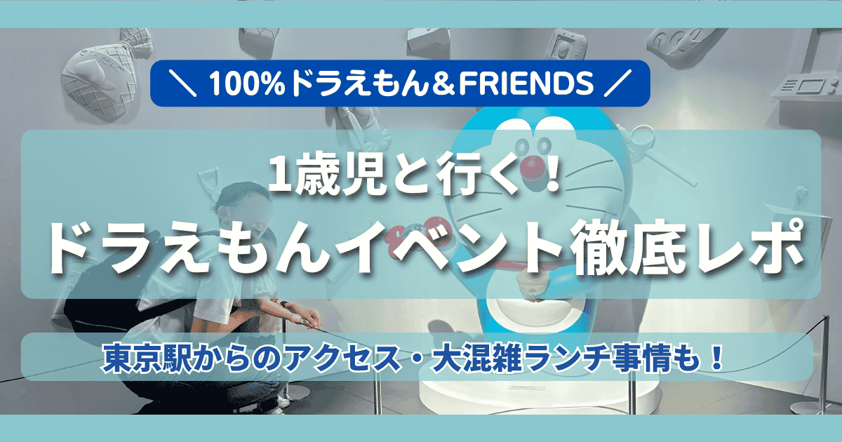 「100％ドラえもん＆FRIENDS（東京ドリームパーク）」の1歳児連れ体験レポ記事のアイキャッチ画像。背景は「まんがワールド展」でベビーカーの横に座るパパと笑顔の娘の写真。中央に白文字で「1歳児と行く！ドラえもんイベント徹底レポ」と書かれており、上下に「東京駅からのアクセス・大混雑ランチ事情も！」の文字が入っている。