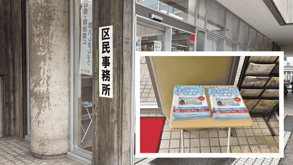 足立区保塚区民事務所の入り口にある「区民事務所」と書かれた看板と、風除室内のテーブルに山積みにされている「足立区商店街応援券」の配布用チラシ(専用はがき)の様子。